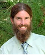 A man with a beard in a green shirt and tie prioritizes optimal health and follows a vegan lifestyle, emphasizing insulin management.
