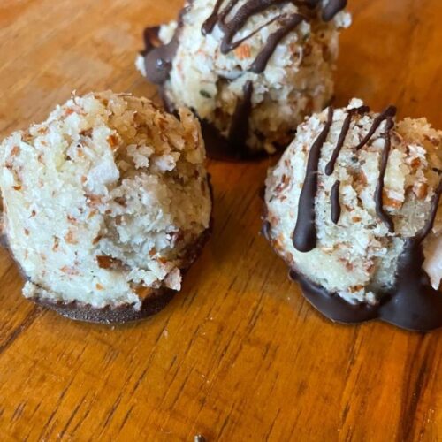 Three coconut macaroons with chocolate bases and drizzled chocolate on top, displayed on a wooden table.