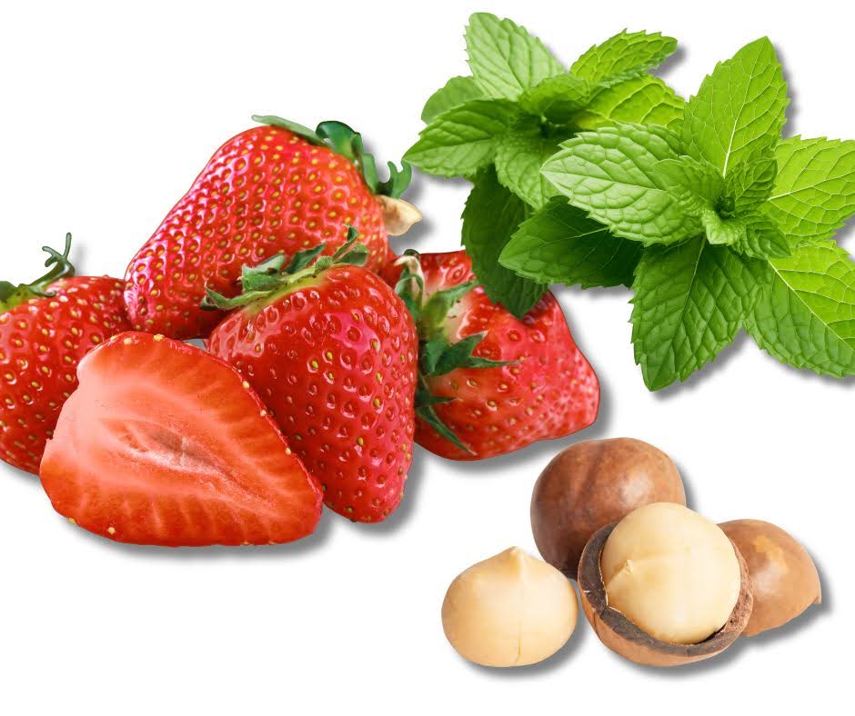 Several fresh strawberries, a sprig of mint leaves, and a few whole and cracked macadamia nuts are artfully arranged on a white background, evoking the vibrant ingredients of a classic Strawberry Parfait.