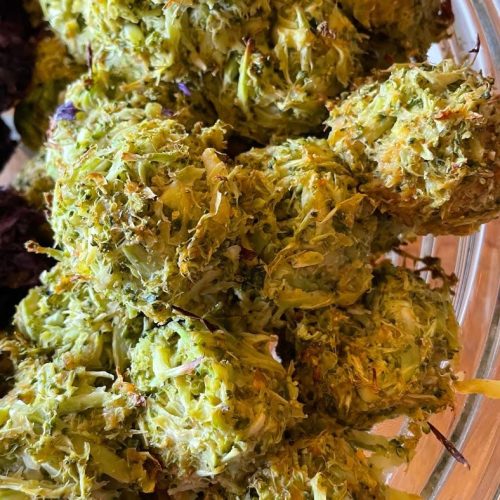 A close-up of several green, leafy balls of food in a glass bowl, resembling vegetable or herb fritters with a rough, textured surface—perfect alongside spicy lentil flatbreads.