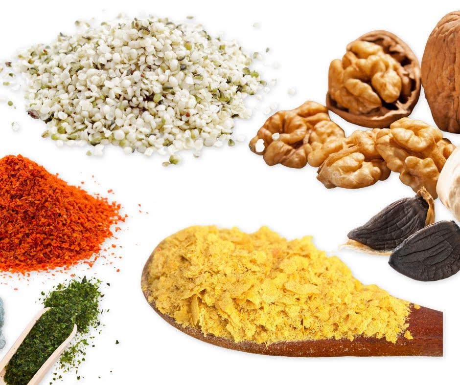 Various vegan parmesan ingredients on a white background, perfect for topping Cheezy Broccoli Bites—hemp seeds, walnuts, nutritional yeast, dried parsley, chili flakes, garlic, and a wooden spoon holding golden nutritional yeast.