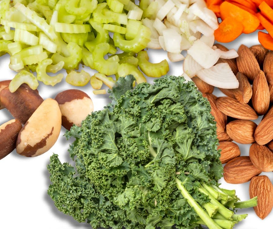 A mix of healthy foods including chopped celery, onions, carrots, whole Brazil nuts, almonds, fresh kale, and a splash of Almond Hemp Seed Milk arranged on a white background.