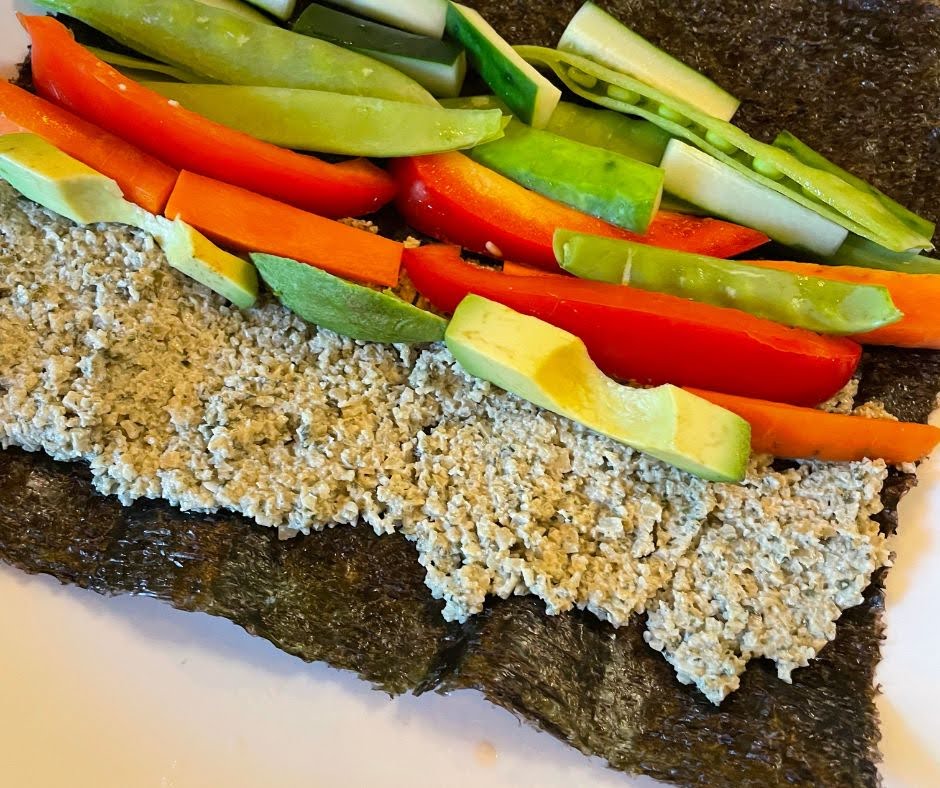 A sheet of seaweed topped with a layer of spread, sliced avocado, red bell pepper, carrot, and cucumber strips—this veggie sushi wrap is packed with the vibrant flavors and nutrients found in a Hormone-Happy Salad.
