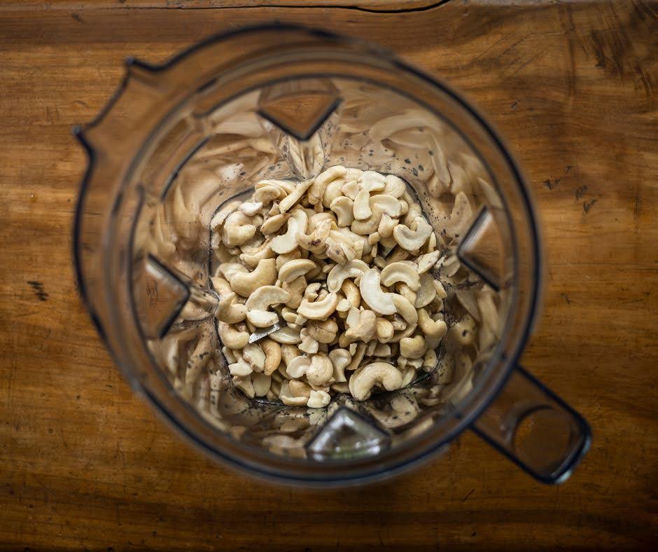 A top-down view of raw cashew nuts inside a clear blender jar, placed on a wooden surface—perfect for crafting smoothies or pairing with Adrenal Energy Tea.