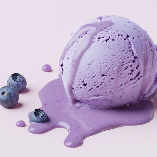 A scoop of melting purple blueberry ice cream sits on a pale pink surface, with two fresh blueberries nearby and purple drips spreading around.