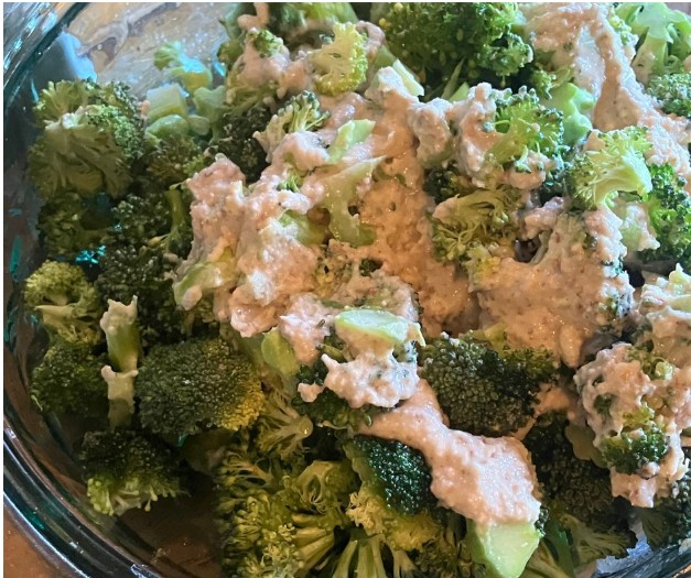A close-up of fresh broccoli florets in a bowl, topped with a thick, creamy sauce or dressing.