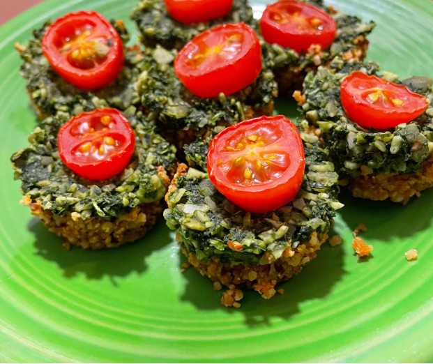 Six small spinach and grain mini casseroles are topped with halved cherry tomatoes and arranged on a bright green plate.
