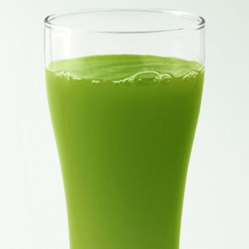 A clear glass filled with bright green juice, shown against a plain white background.