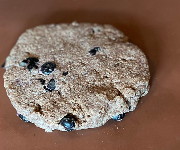 A round, textured blueberry cookie on a brown surface.